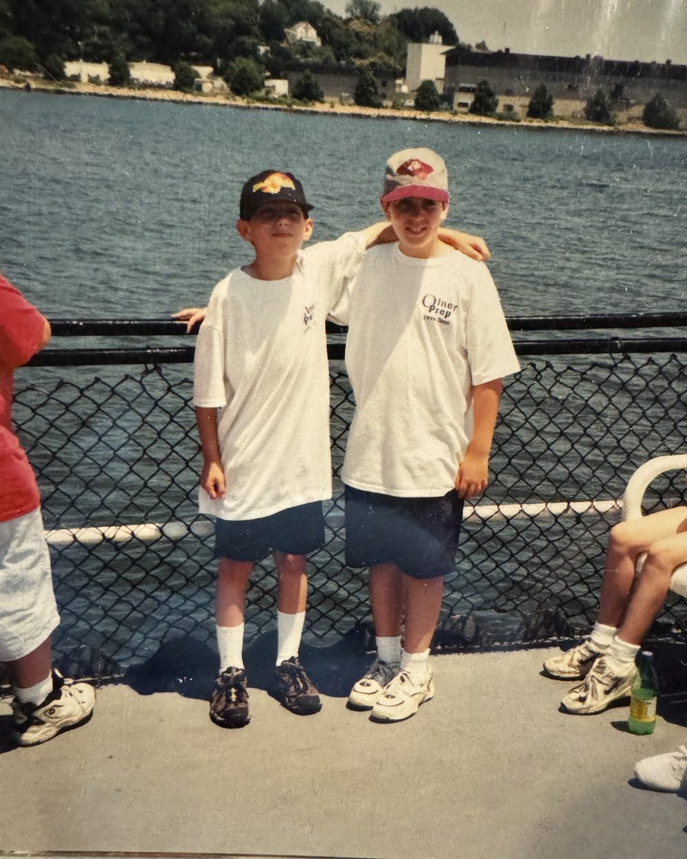 Two boys in matching Olney Prep T-shirts on a ferry deck, with water and a shoreline behind them