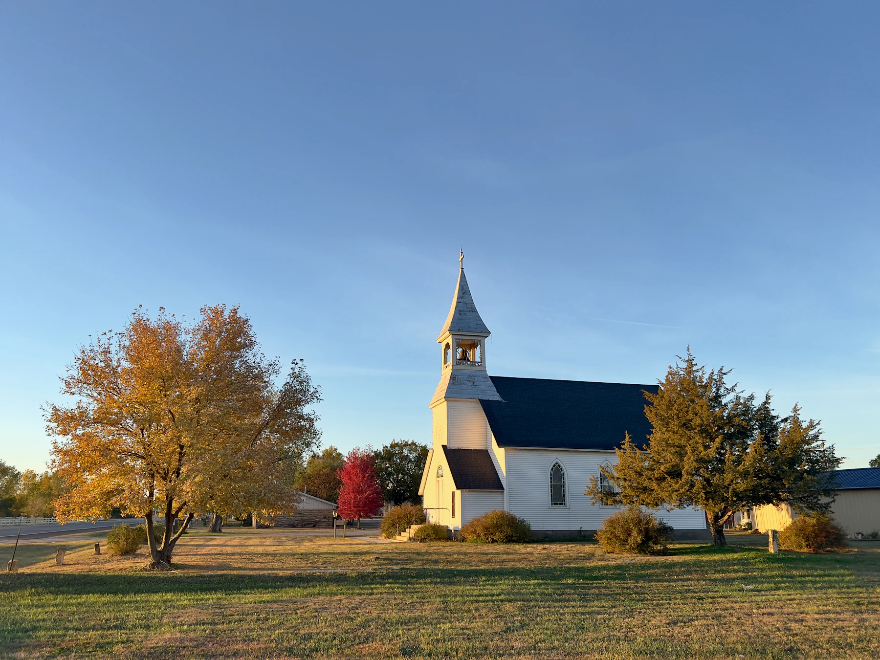 A white wood church with a steeple and an autumn maple out front